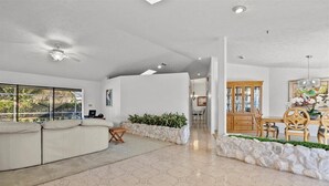 A spacious living area with a white sofa, a dining table with chairs, and a stone planter with plants. - Riverside Retreat: 4BR/3BA with Private Dock and Boat Lift (Stuart)