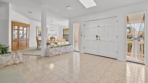 A spacious living area with a large white door, a dining table with chairs, and a cabinet with glass doors. - Riverside Retreat: 4BR/3BA with Private Dock and Boat Lift (Stuart)