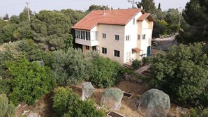 A two-story building with a red-tiled roof, surrounded by dense greenery and trees.