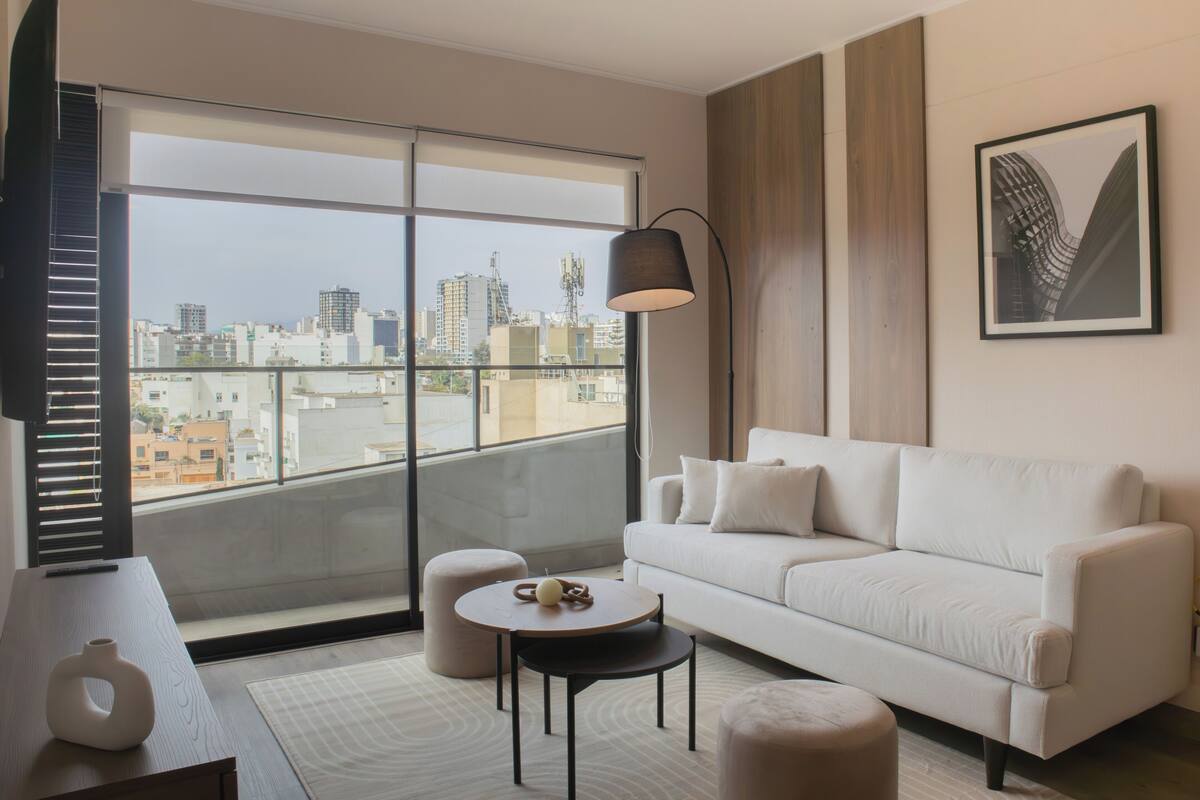 Ein modernes Wohnzimmer mit einem weißen Sofa, einem runden Couchtisch und einem großen Fenster mit Blick auf die Stadt.