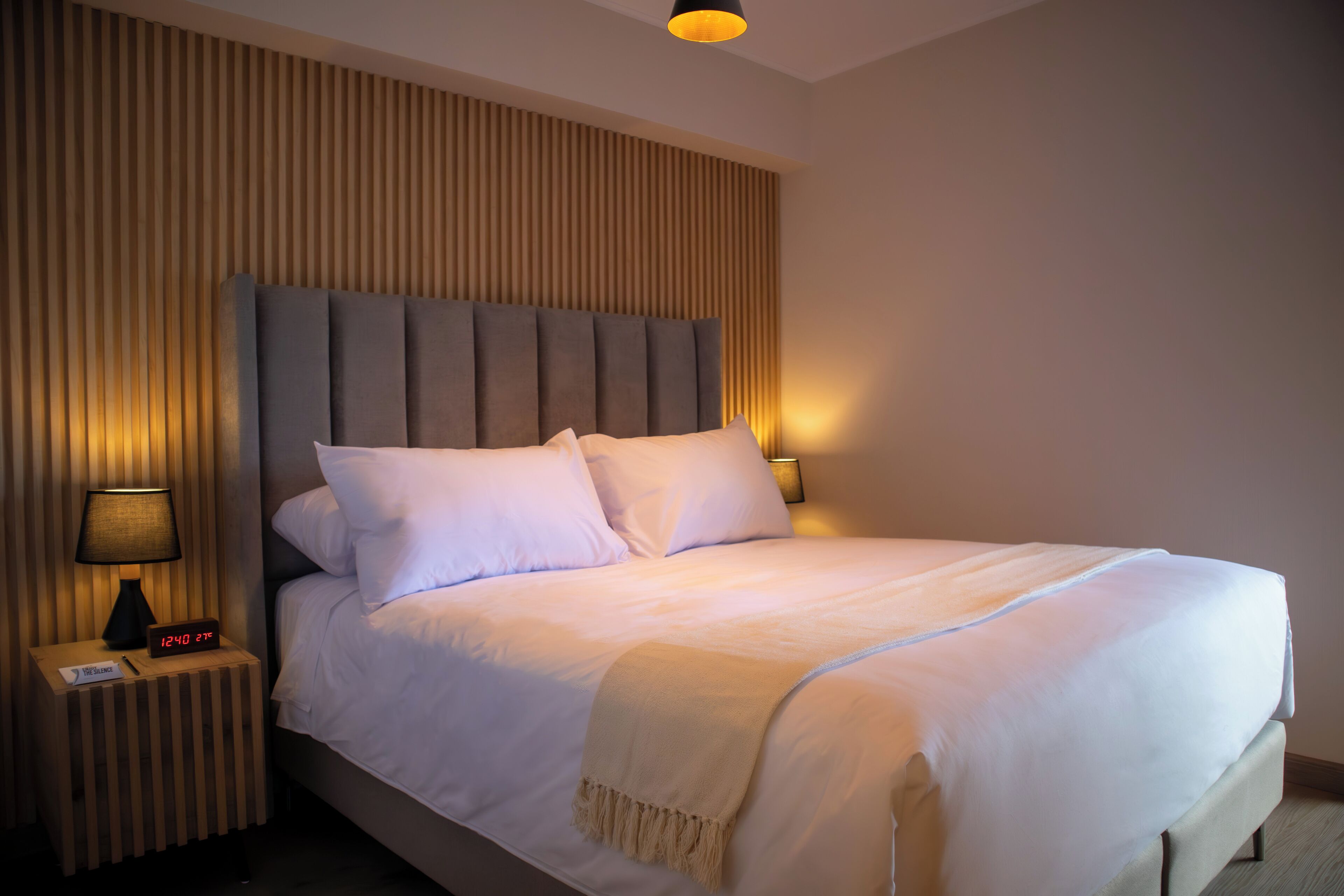 A neatly made bed with a headboard, two bedside lamps, and a digital clock on a bedside table.