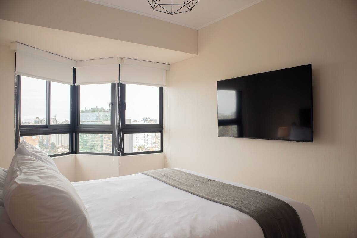 Ein Hotelzimmer mit Bett, großem Fenster und einem an der Wand befestigten Flachbildfernseher.