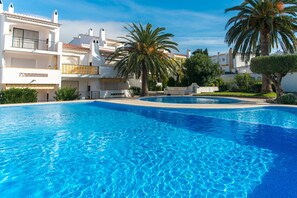 A swimming pool with clear blue water, surrounded by white buildings with balconies and palm trees. - WELCS APARTAMENTO 201 EMP con TERRAZA (Rosas / Roses)