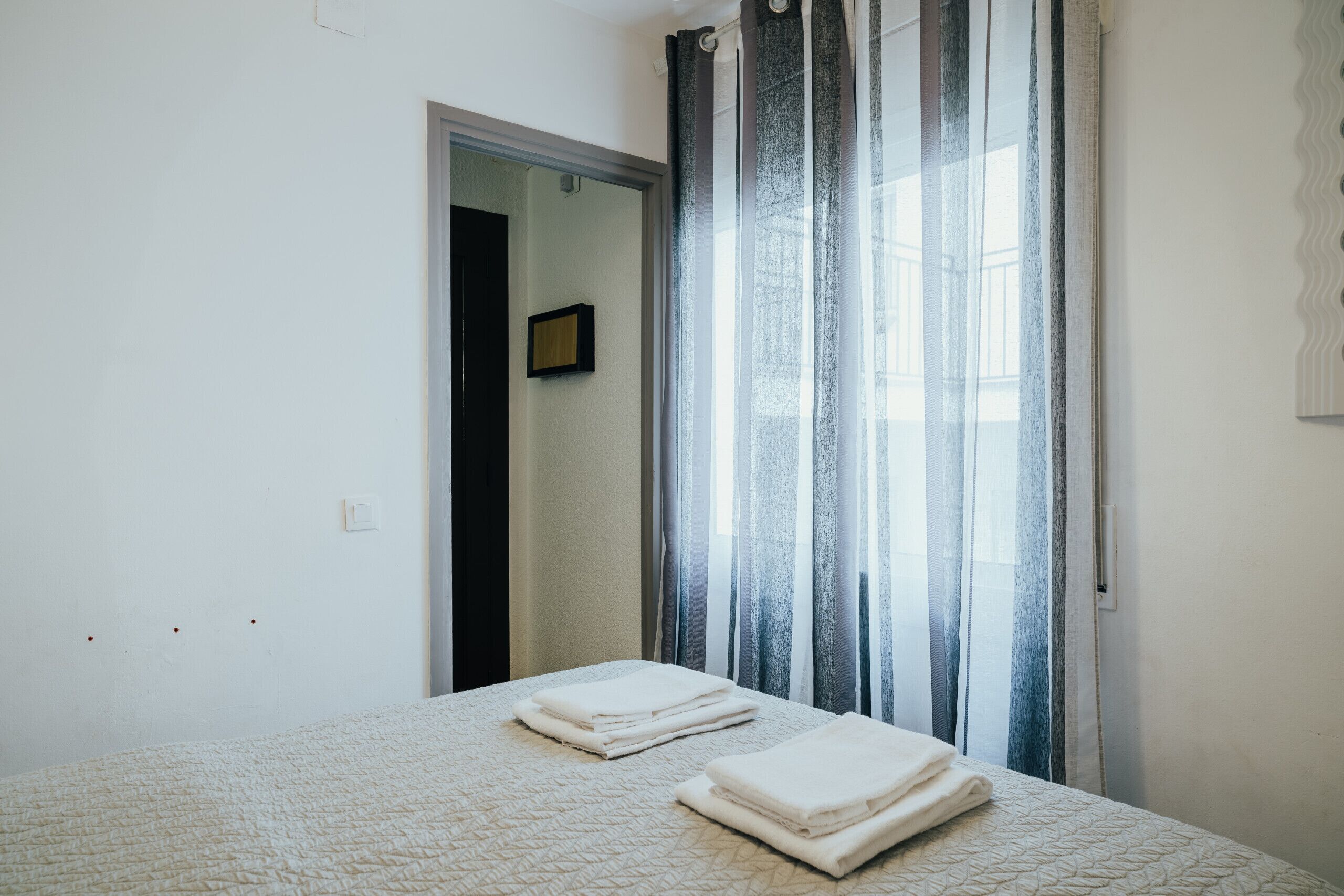 A hotel room with a bed, a door leading to another room, and sheer curtains.