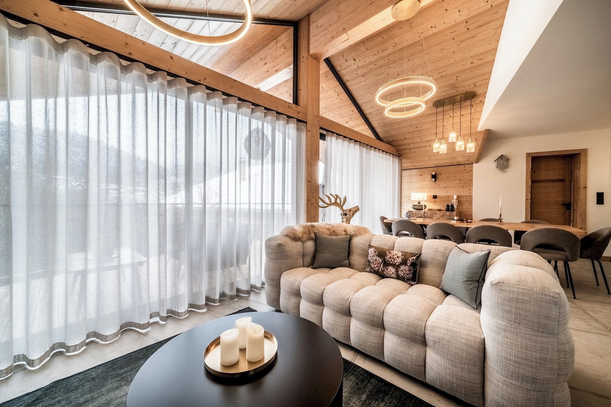 A modern living room with a large sofa, a coffee table with candles, and a dining area in the background.