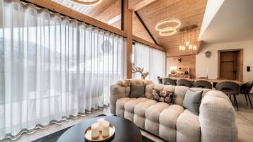 A modern living room with a large sofa, a coffee table with candles, and a dining area in the background.