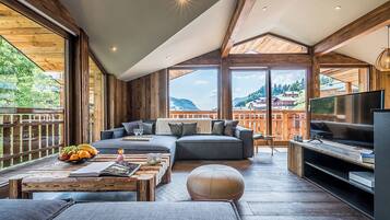 A modern living room with a large sofa, a coffee table with fruits, and a TV.