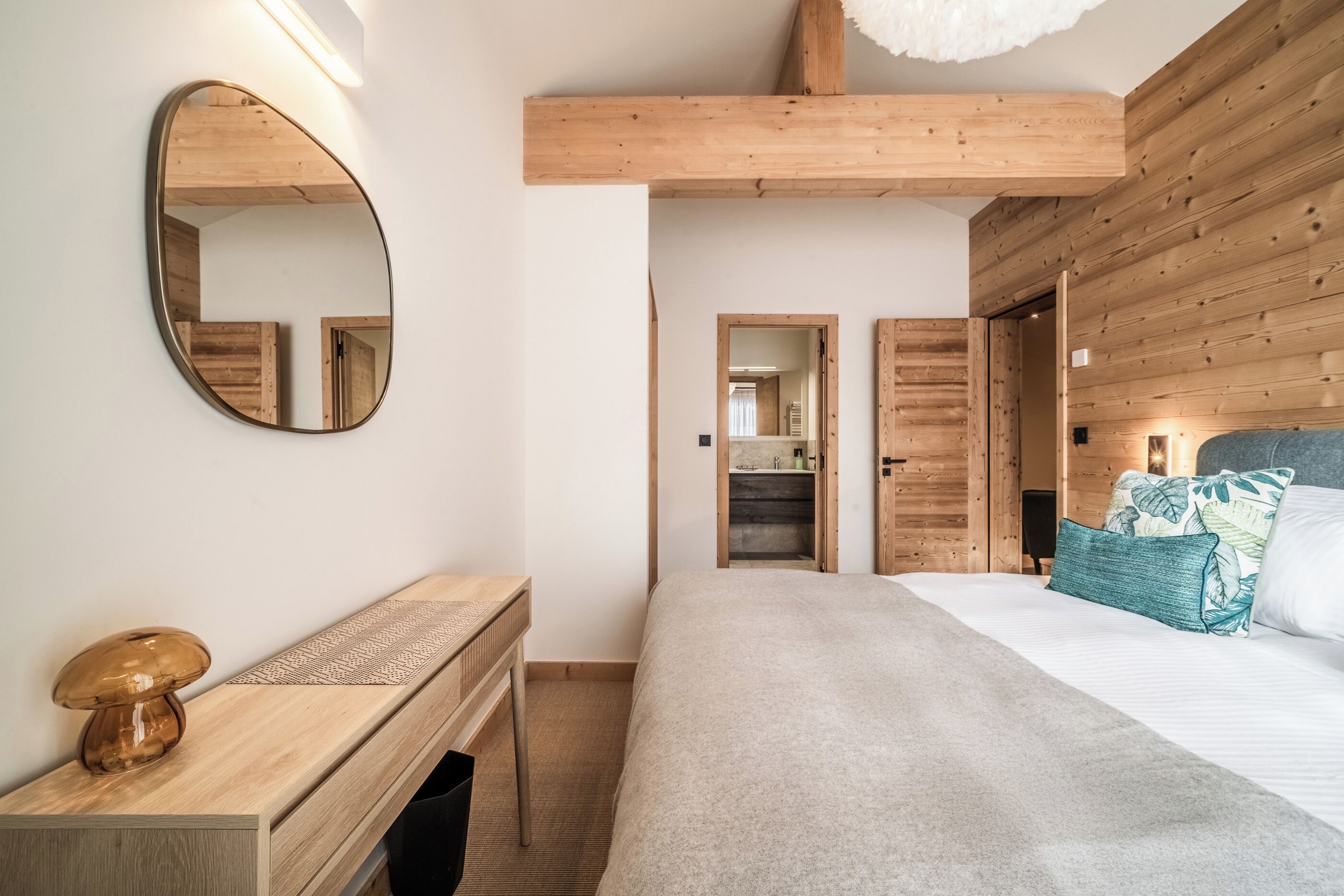 A bedroom with a wooden headboard, a large mirror, a bedside table with a lamp, and a bed with a patterned throw.