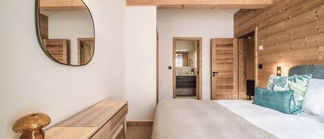 A bedroom with a wooden headboard, a large mirror, a bedside table with a lamp, and a bed with a patterned throw.