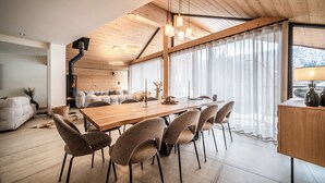 Zona pranzo moderna con tavolo e sedie in legno, camino e ampie finestre con tende leggere.