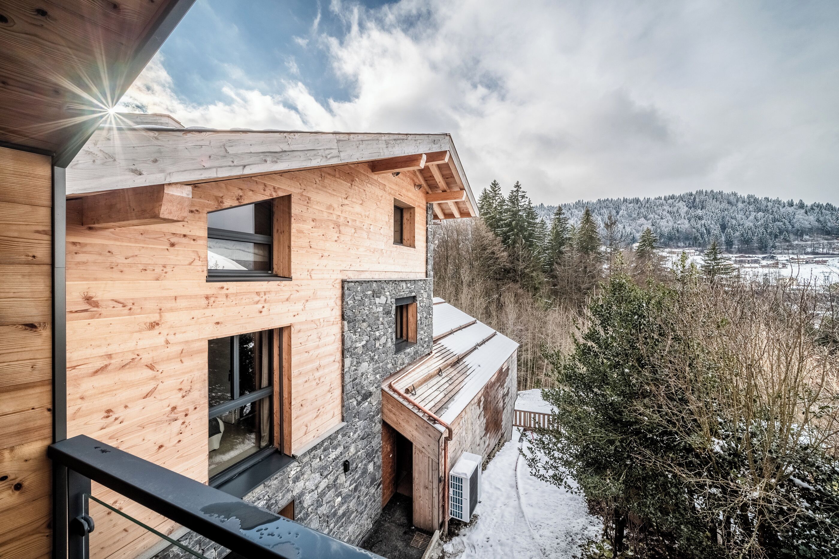 A modern wooden cabin with large windows and a view of a snowy landscape.