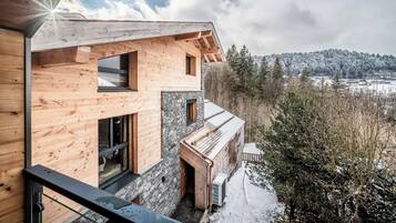 A modern wooden cabin with large windows and a view of a snowy landscape.