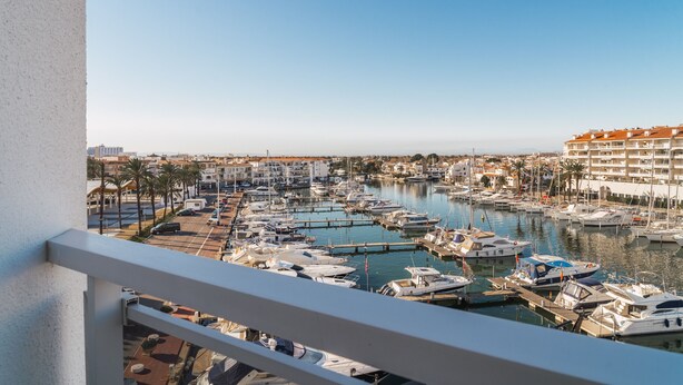 A marina with numerous boats docked, surrounded by buildings and palm trees.