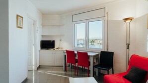 A modern kitchen with white cabinets, a dining area with red chairs, a red sofa, and a large window with a city view.