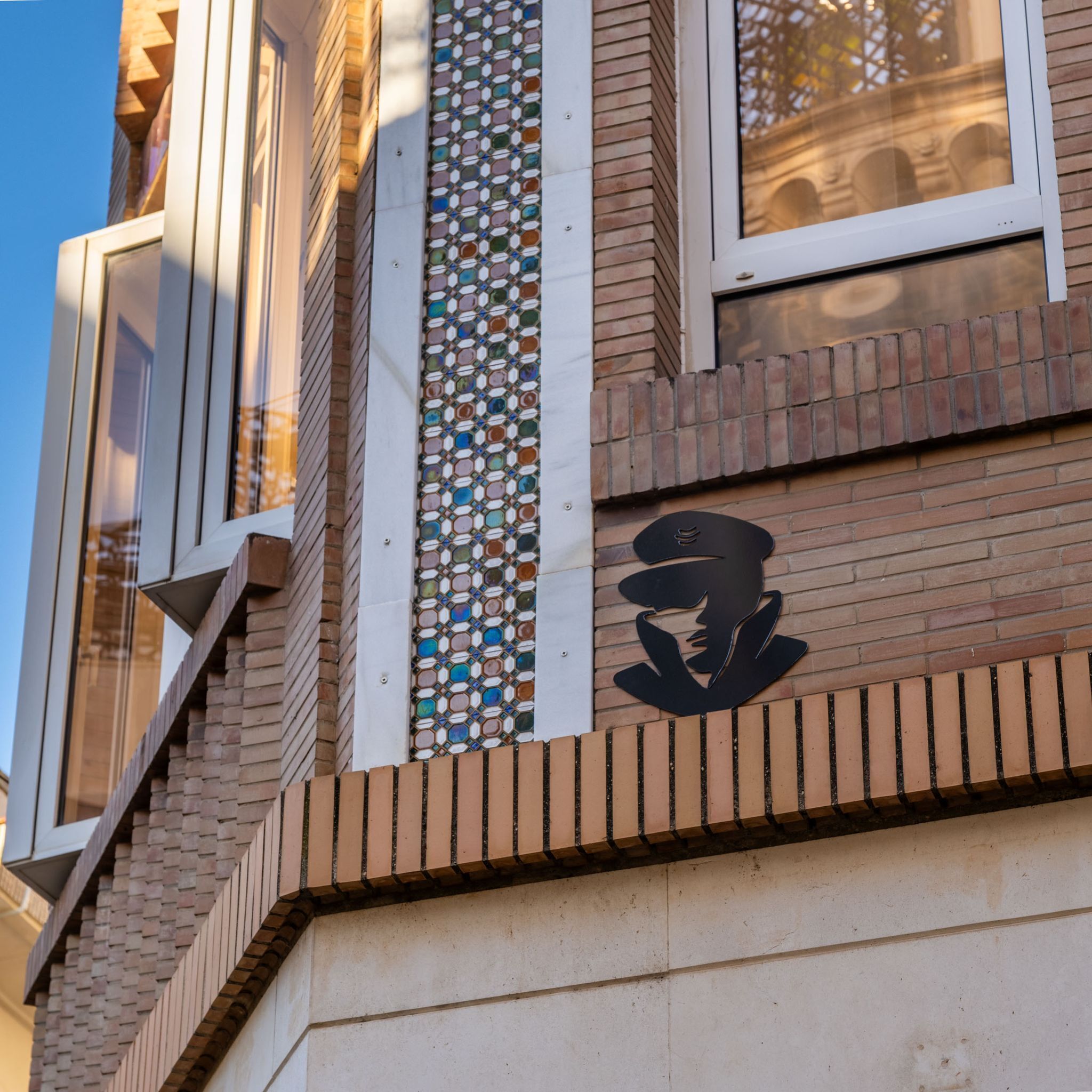 Fachada de edificio con una columna de baldosas estampadas, un logotipo negro y una escalera de ladrillo.