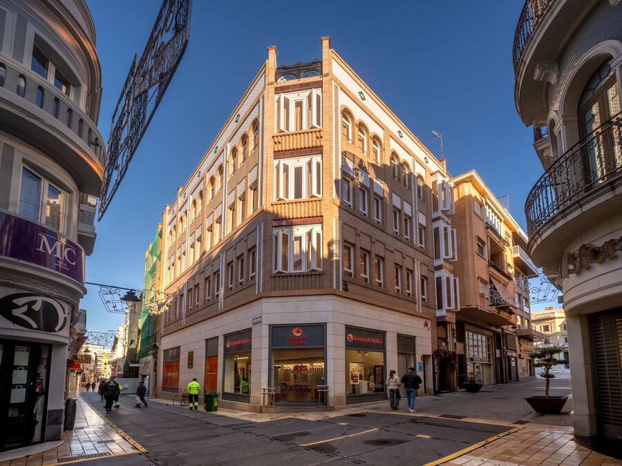 Un edificio en esquina con varios pisos, que presenta locales comerciales en la planta baja.