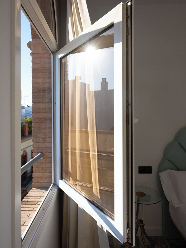 Una habitación con ventana que da a un edificio de ladrillo y un balcón.