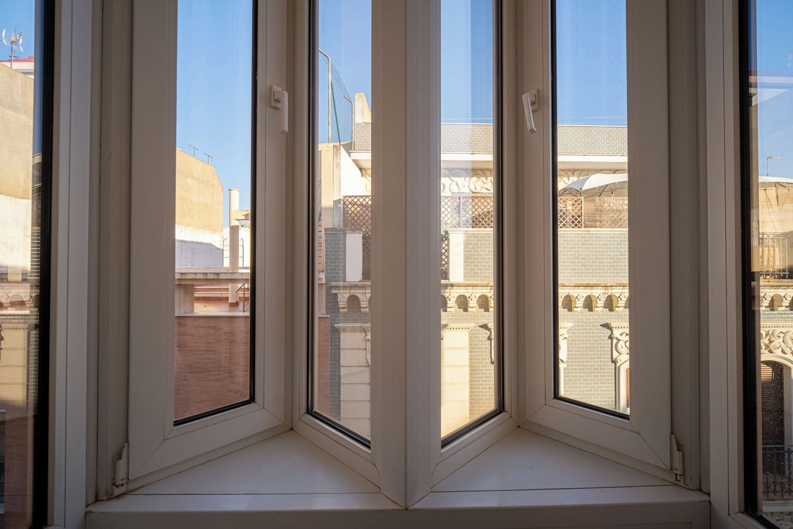 Una ventana de esquina con vista a un edificio de fachada de ladrillo y ventanas arqueadas.