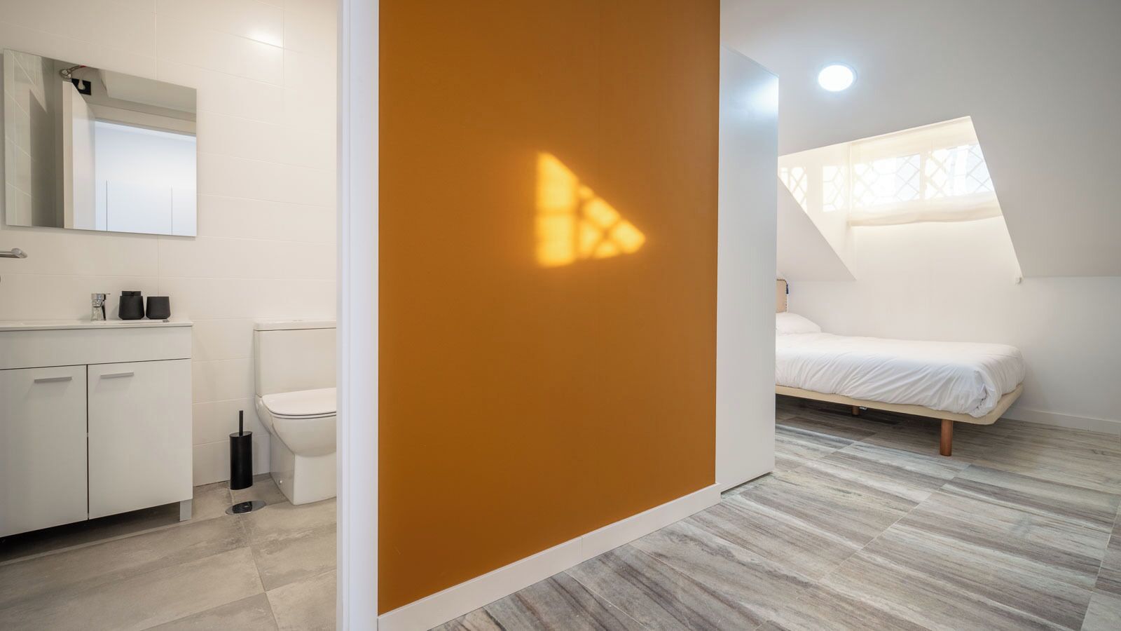 A modern bedroom with a bed, a bathroom with a toilet, and a large window.