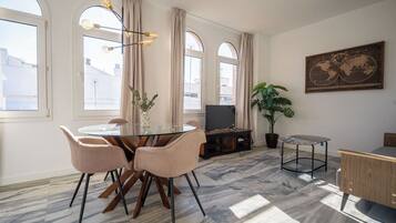 Un salon moderne avec une table à manger en verre, des rideaux beiges, une grande plante en pot et une carte du monde accrochée au mur.