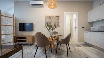 Una cocina moderna con armarios blancos, microondas y un comedor con mesa de vidrio y dos sillas.