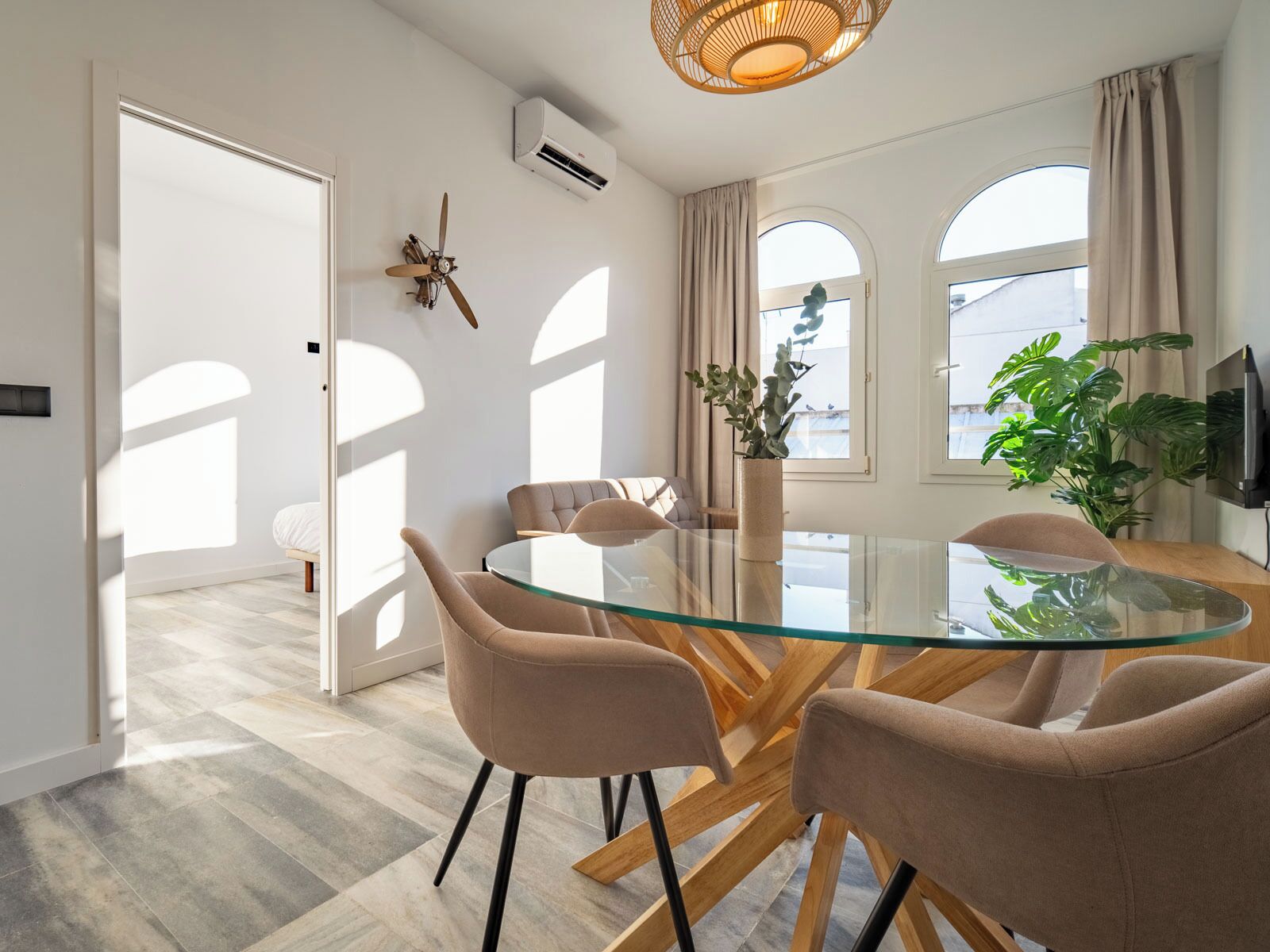 Un comedor moderno con una mesa de vidrio, sillas color beige y un ventilador de techo.