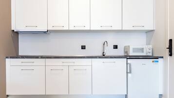 Una cocina moderna con armarios blancos, microondas integrado y refrigerador.