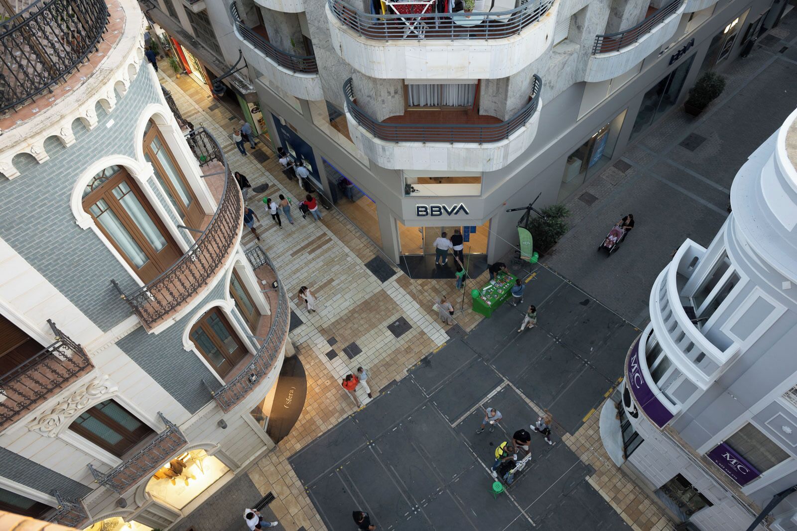 A multi-story building with a BBVA bank on the ground floor, featuring a central courtyard with a green table and chairs.