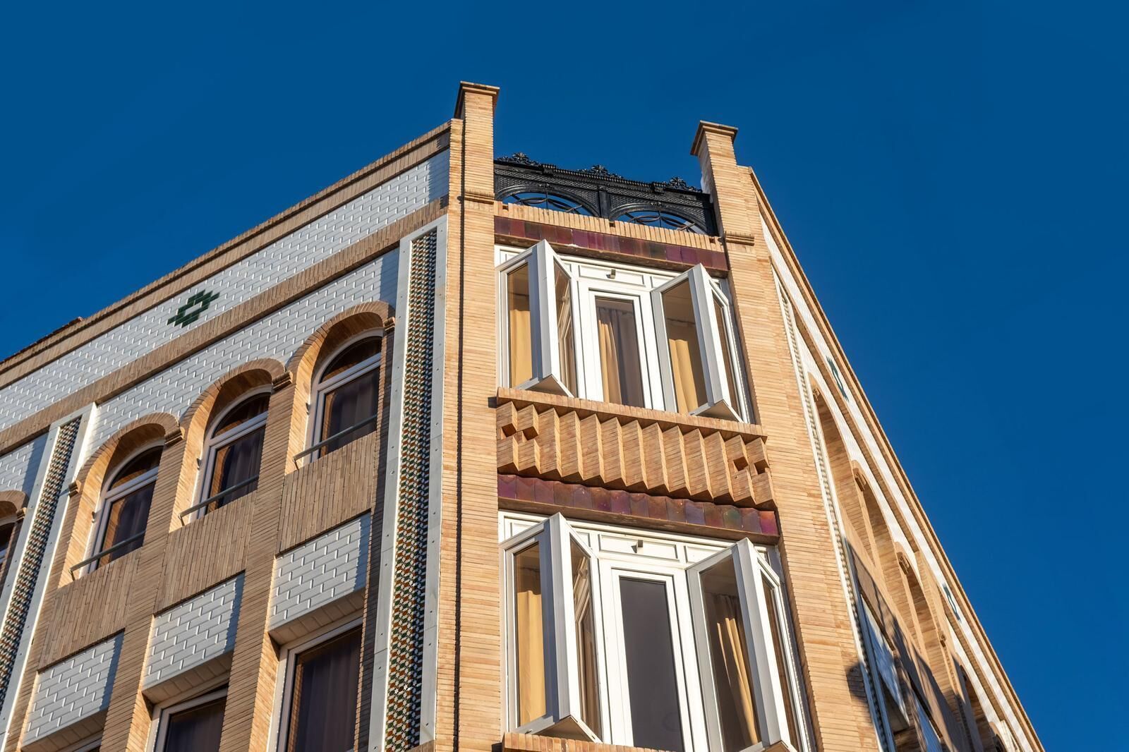 A corner of a building with a brick facade, large windows, and a decorative metal railing.