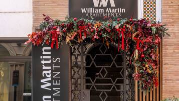 Een gebouwentree met een bordje voor William Martin Apartments, met een decoratieve krans en een geometrisch metalen hek.