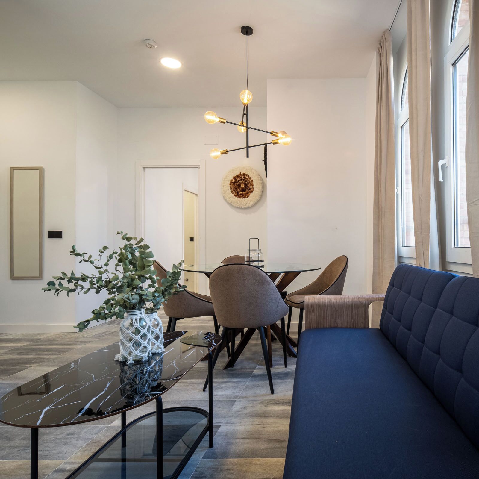 Una sala de estar moderna con un sofá, una mesa de comedor con sillas, una mesa de centro de vidrio y una lámpara colgante.
