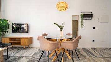 Een moderne eethoek met een ronde glazen tafel, twee comfortabele stoelen, een houten dressoir, een grote spiegel, een hangplant en een luchtzuiveraar aan de muur.