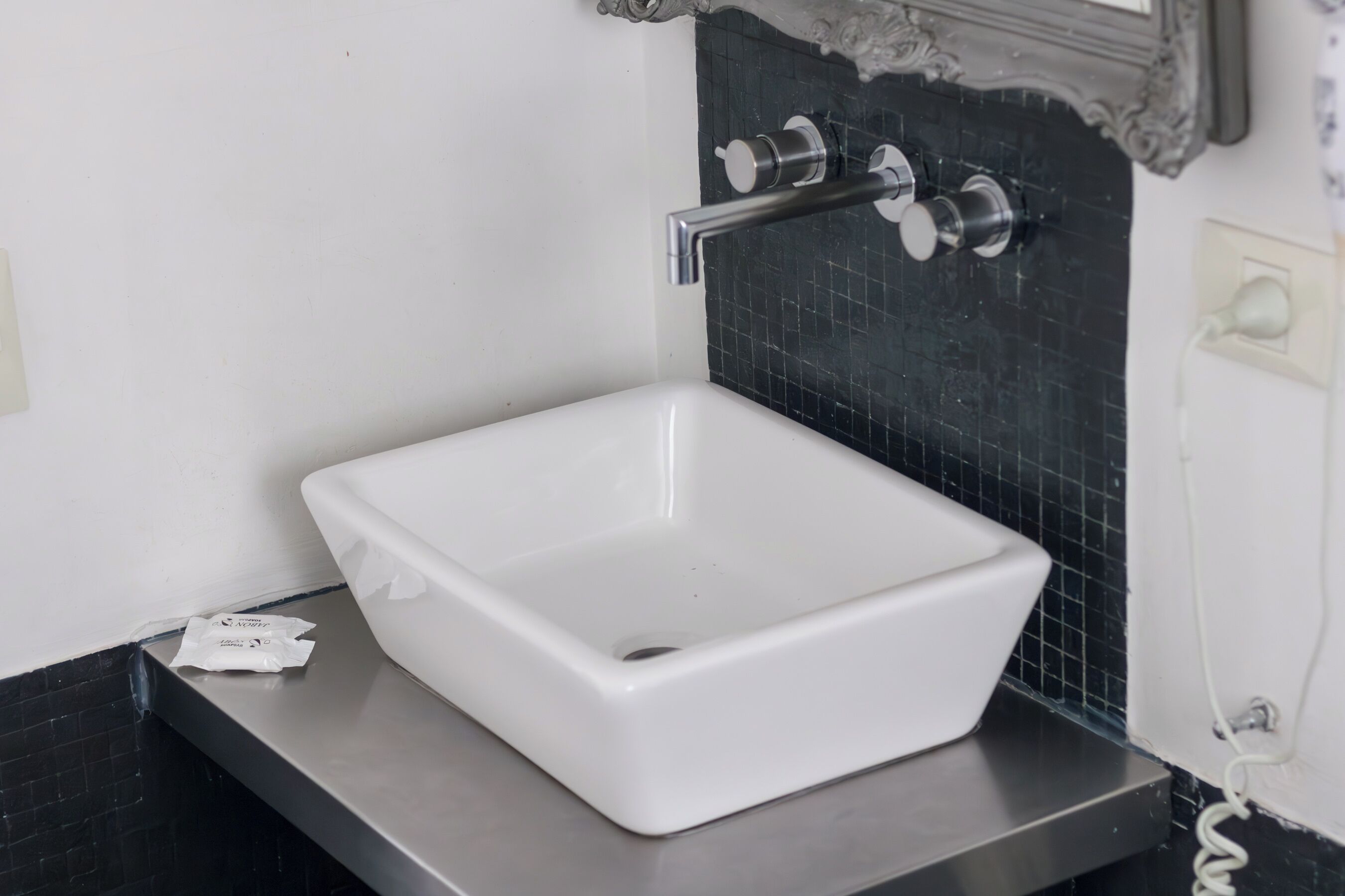 Ein weißes, rechteckiges Waschbecken mit einem modernen Wasserhahn auf einer schwarzen Arbeitsplatte.