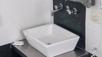 Ein weißes, rechteckiges Waschbecken mit einem modernen Wasserhahn auf einer schwarzen Arbeitsplatte.