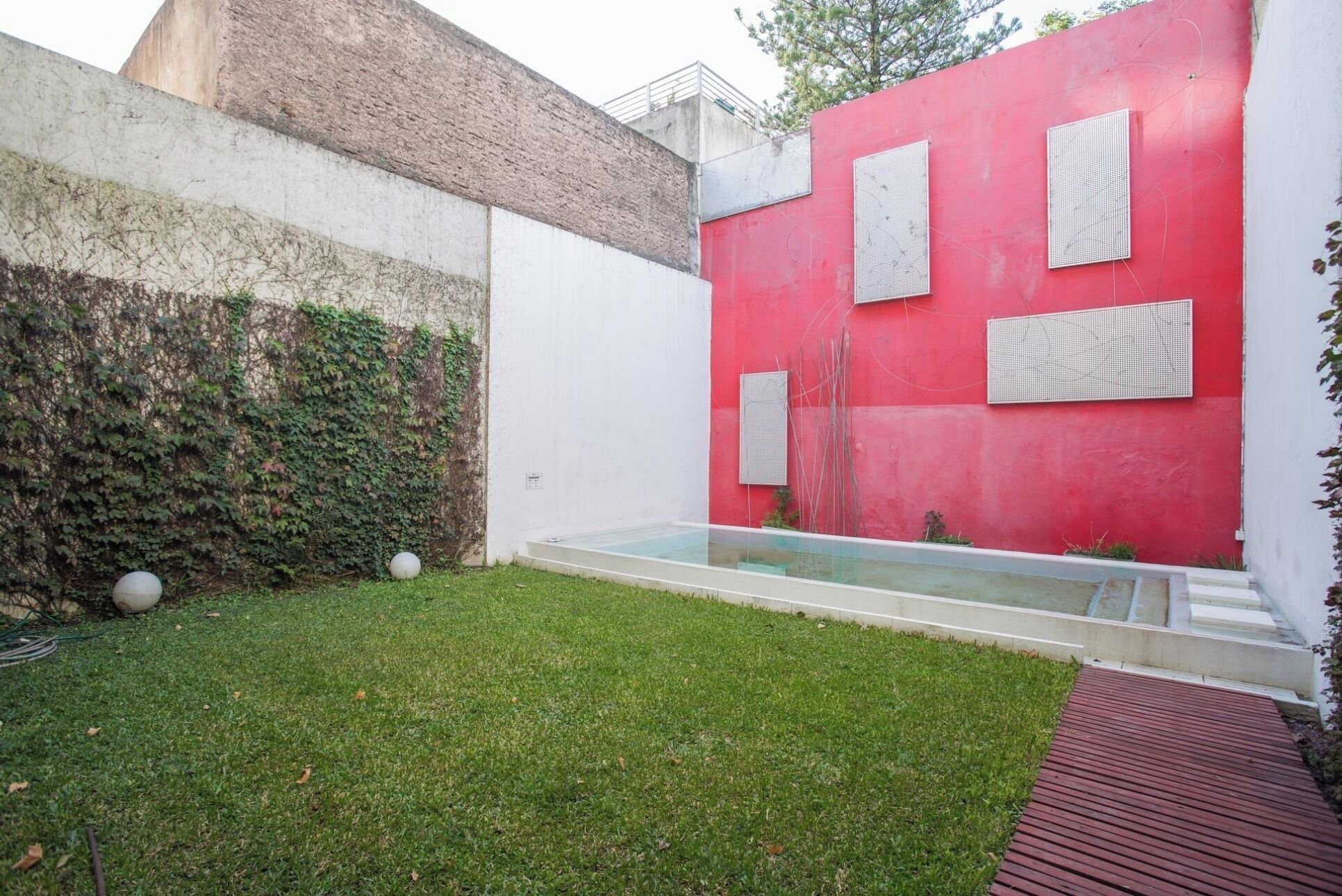 A modern outdoor space with a red wall, a glass water feature, and a grassy area.