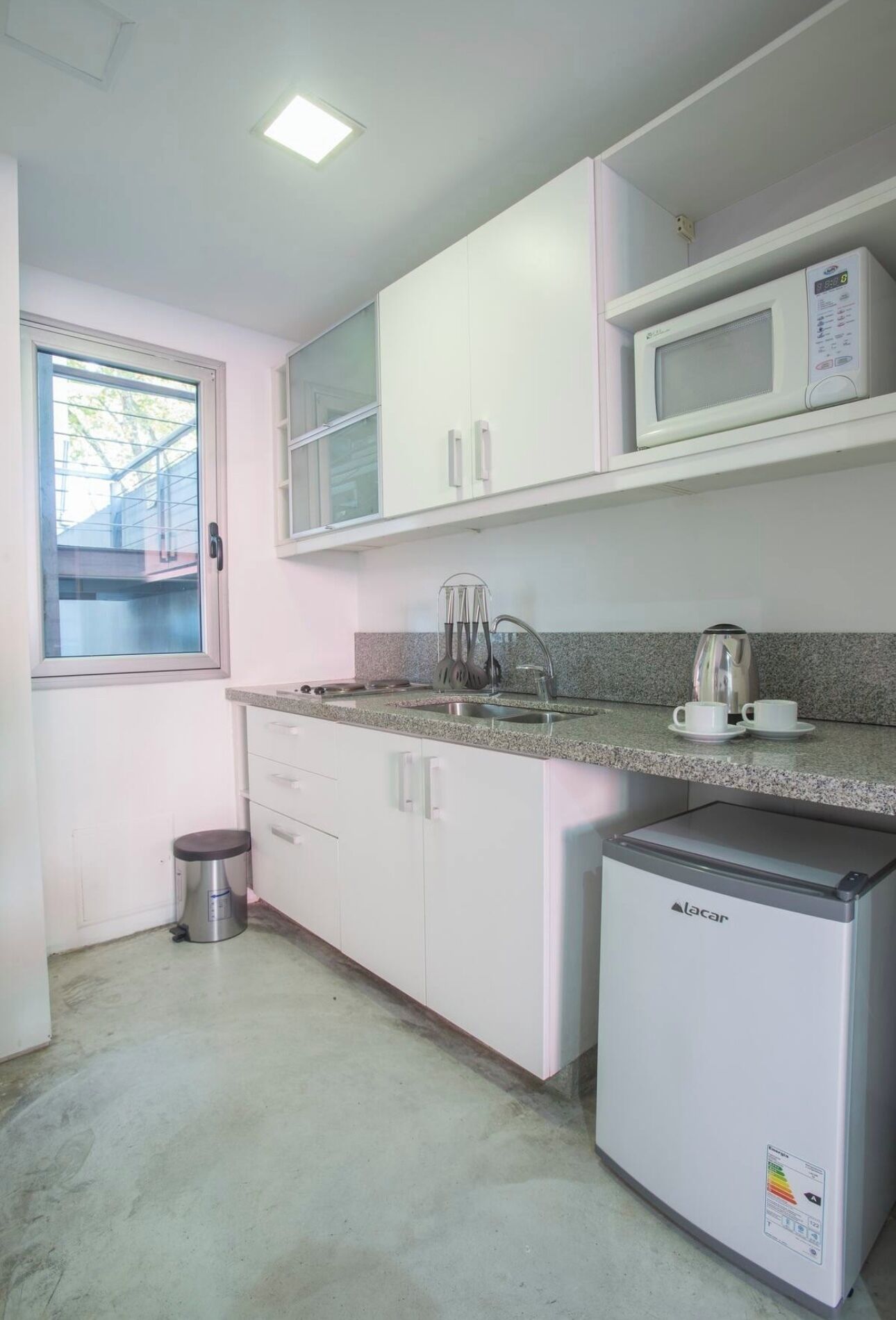 A compact kitchen with white cabinets, a microwave, a coffee maker, and a refrigerator.