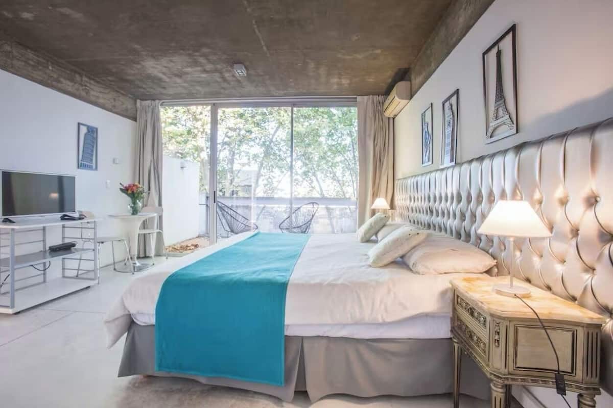 A modern bedroom with a large bed, a television, a desk, and a balcony with chairs.