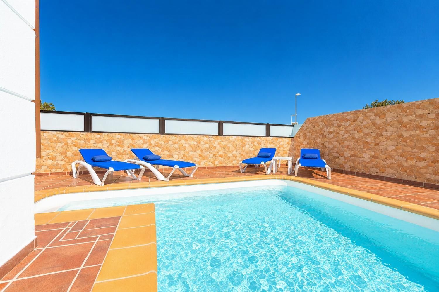A swimming pool with blue lounge chairs and a stone wall.