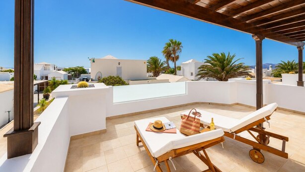 Una terrazza sul tetto con una pergola, un tavolo con una sedia e vista sugli edifici e palme circostanti.