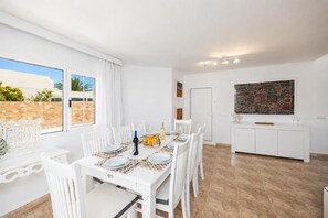A dining area with a table set for six, a kitchen area, and a large window with a view of greenery. - Villa Eugina - Three Bedroom Villa, Sleeps 6 (Tias)