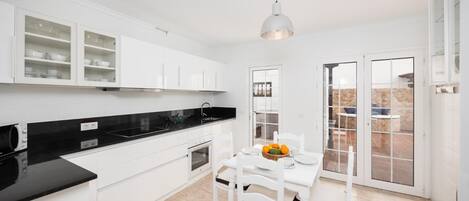 A modern kitchen with white cabinets, a black countertop, and a dining area with a table and chairs.