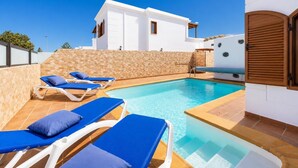 Un'area piscina con lettini e un edificio bianco con parete in pietra.