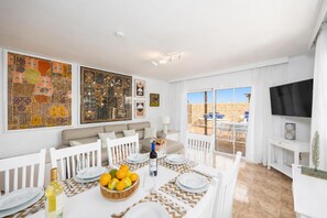 A dining area with a table set for four, a sofa, a TV, and a balcony with a view.