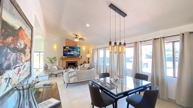 A modern living room with a fireplace, a large painting, and a dining area with a glass table.