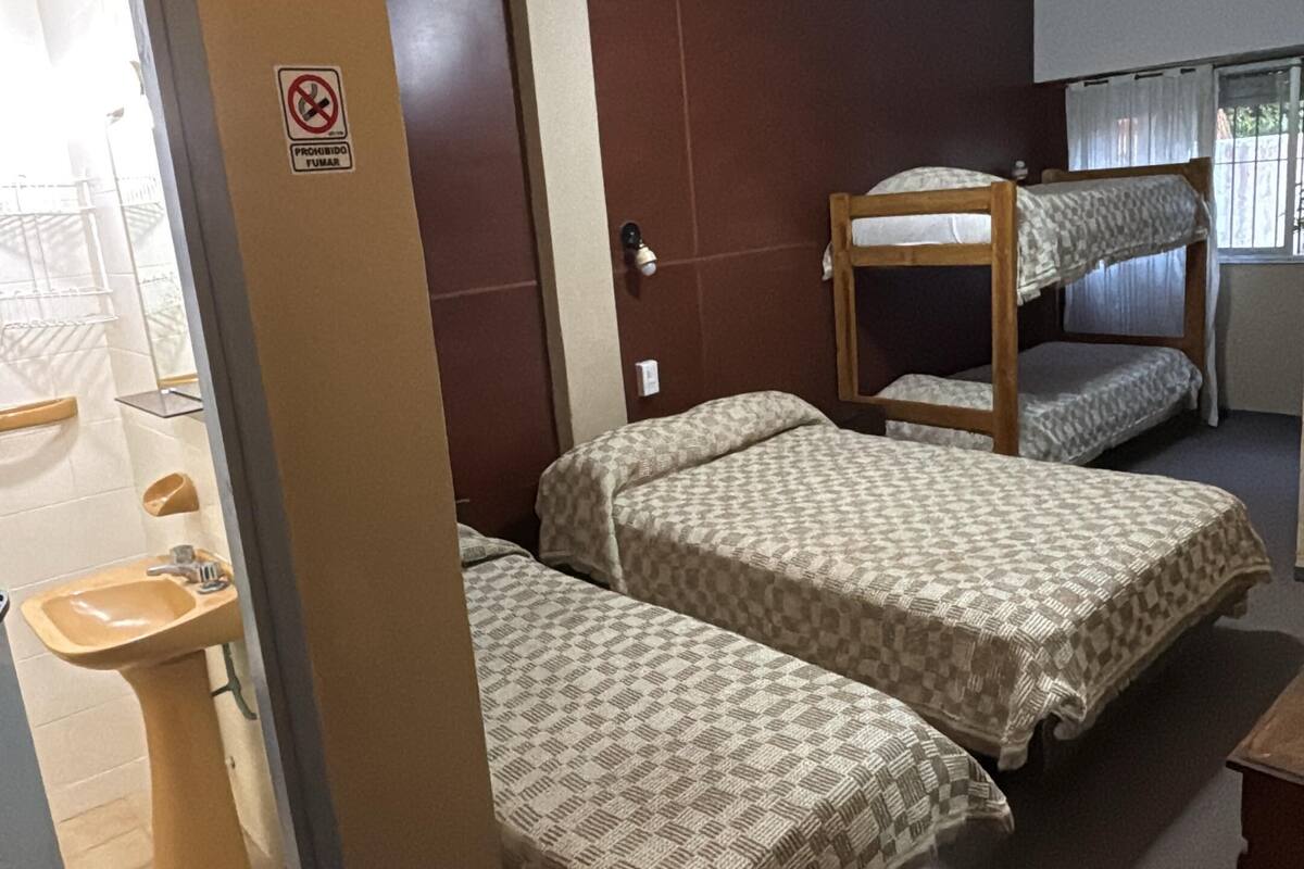 Une chambre avec des lits superposés, un ventilateur de plafond, une salle de bain avec un lavabo et un panneau indiquant qu'il est interdit de fumer.