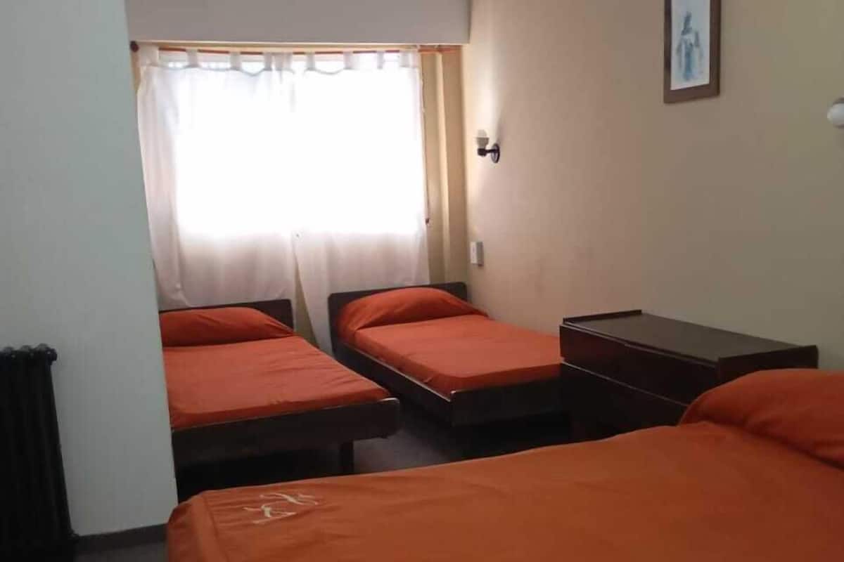 Une chambre avec deux lits simples, une petite table et une fenêtre avec des rideaux.