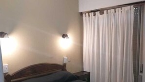 A bedroom with a wooden bed, two wall-mounted lamps, and a window with curtains. - Gran Bahía Resort (San Clemente)