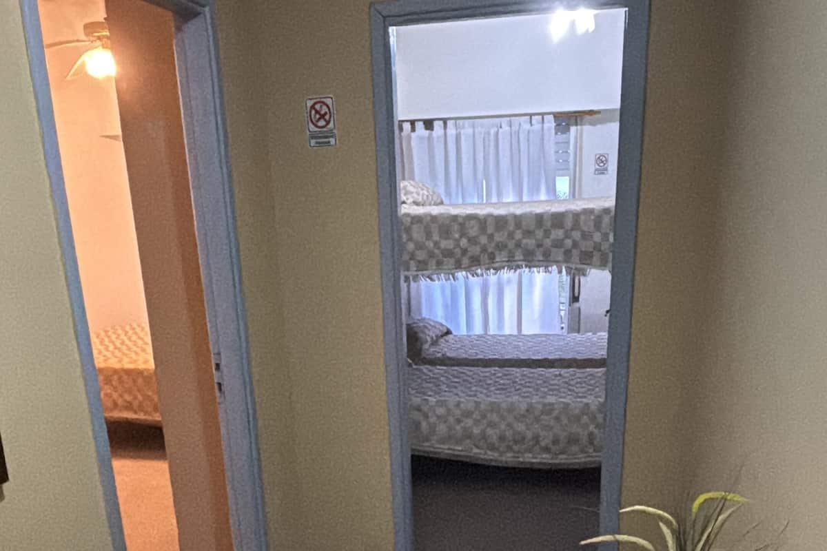 Un couloir étroit, avec en arrière-plan un lit superposé, une table en bois ornée d’une plante et une porte donnant sur une autre pièce.