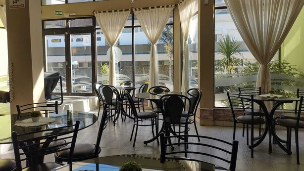 A restaurant with multiple tables and chairs, large windows with curtains, and a view of the street outside. - Gran Bahía Resort (San Clemente)