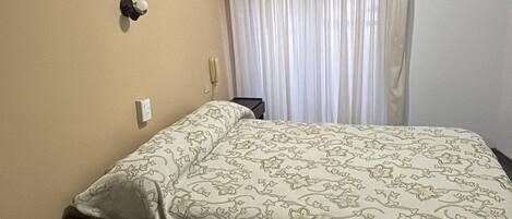 Habitación de hotel con cama, mesita de noche, ventilador de techo y ventana con cortinas.